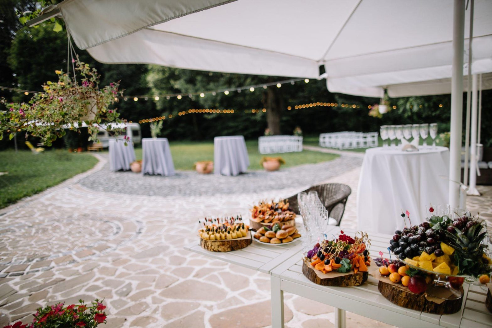 Outdoor wedding setup with appetizers and fruit platters under a canopy.