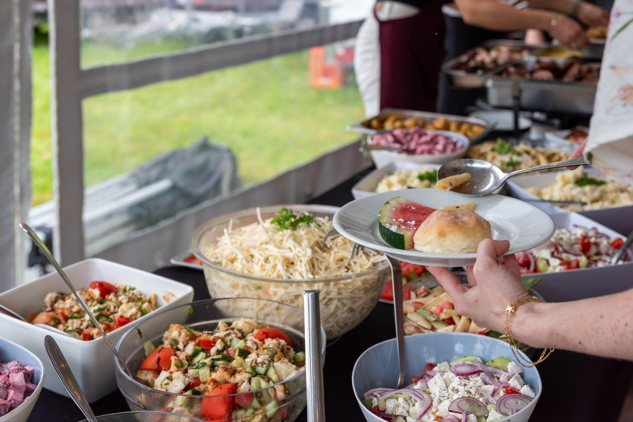 Guest serving salad and bread from an outdoor wedding buffet