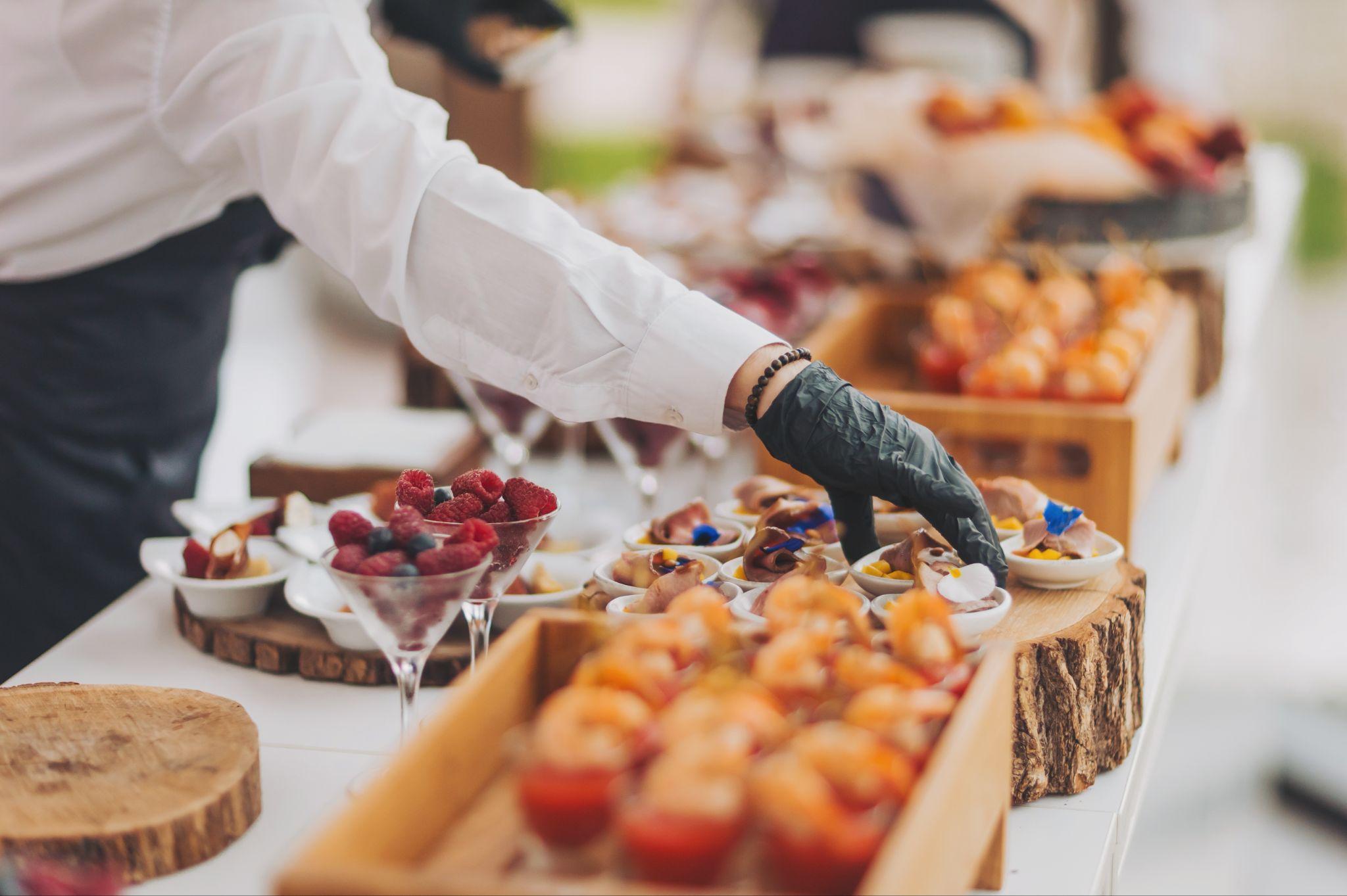 Caterer arranging mini desserts and berry cups on a wedding buffet table.
