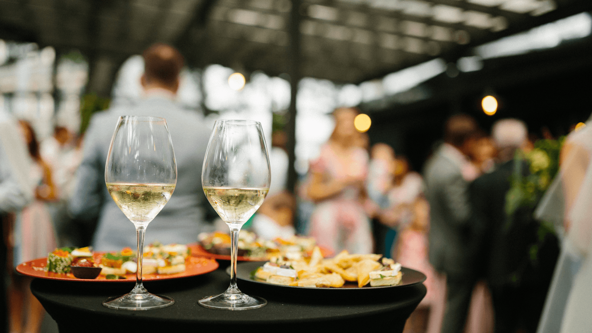 Two wine glasses on a table filled with foods at a catered event