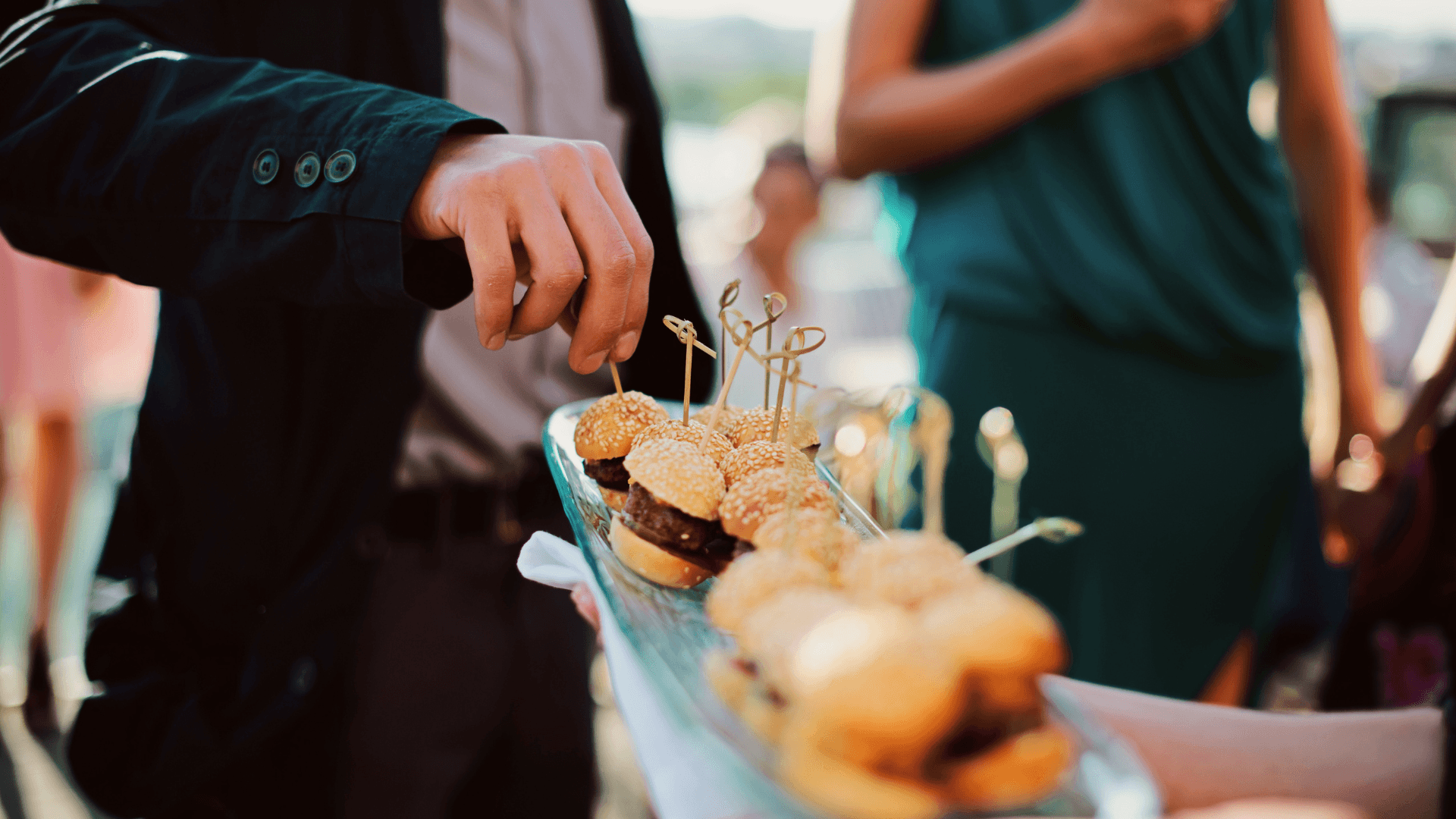 A man picking mini-burgers off of a platter by a waitress