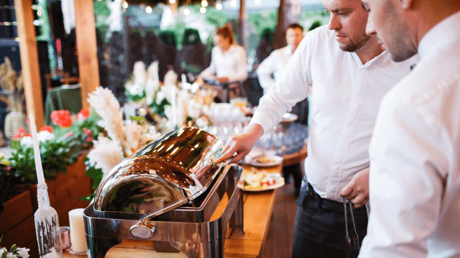 Two waiters opening a pot of food at a catering event